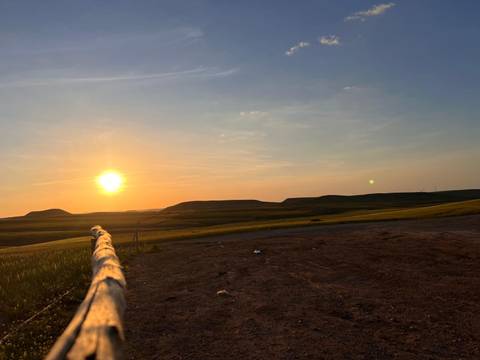       Open rolling plains with low hills and a setting sun casting warm light across the landscape.
  