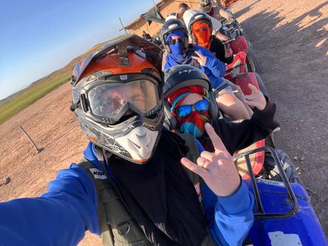       Selfie of helmeted travelers on quad bikes, flashing hand signs before an off-road desert ride.
  