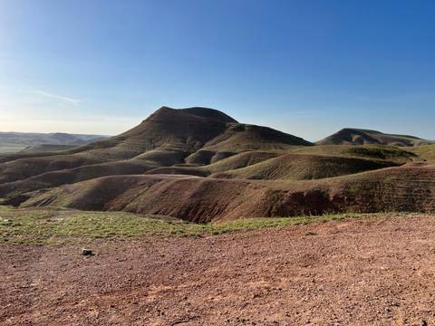       Rugged reddish hills and valleys under a clear blue sky in a semi-arid landscape.
  