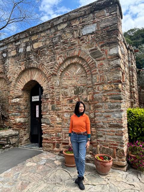       Traveler standing by an ancient brick archway at a historic ruin, wearing an orange sweater.
  