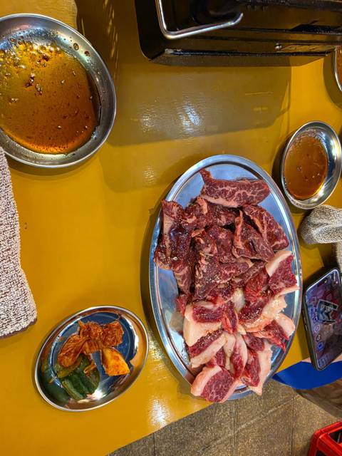       Plate of raw marinated beef slices ready for yakiniku grilling, surrounded by dipping sauces.
  