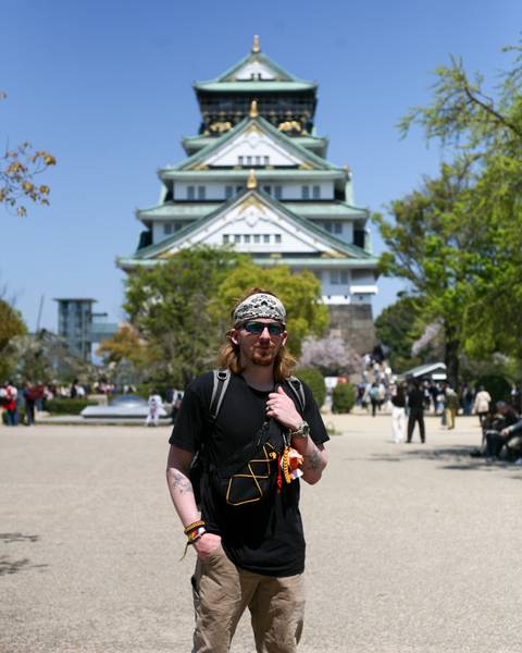       Traveler wearing bandana standing in front of Osaka Castle on a sunny spring day.
  