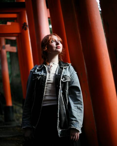       Woman gazing upward among shadowed orange torii pillars.
  