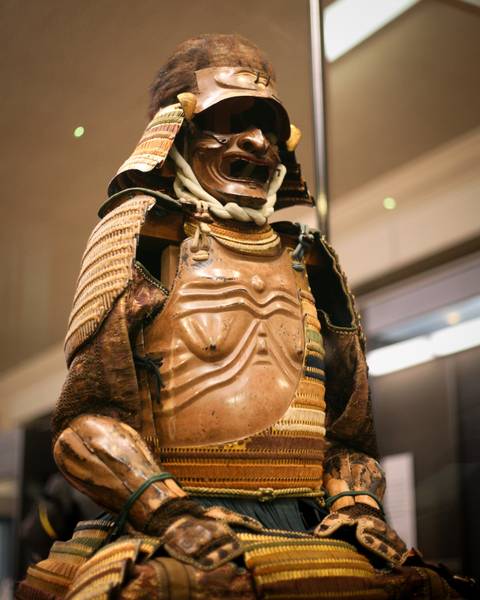       Detailed view of traditional Japanese samurai armor displayed in museum lighting.
  