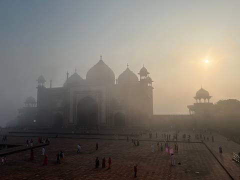       Silhouetted mosque building of Taj complex emerging from sunrise haze with soft sun disc.
  