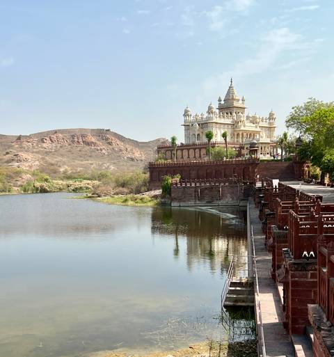       Marble memorial Jaswant Thada by tranquil lake with arid hills in background.
  