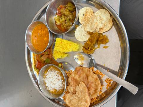       Traditional Indian thali meal served on metal tray with various curries, rice and breads.
  
