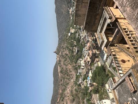       Panoramic view from Amber Fort over rugged hills and clustered village buildings.
  