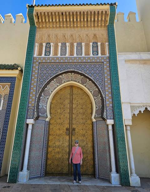       Intricately patterned golden door framed by colorful zellige tilework and horseshoe arch in Fes.
  