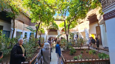       Courtyard garden with orange trees, mosaics and many visitors inside a traditional riad.
  