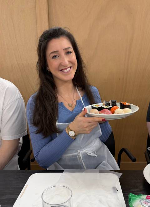       Participant proudly displays a plate of handmade sushi pieces during class.
  