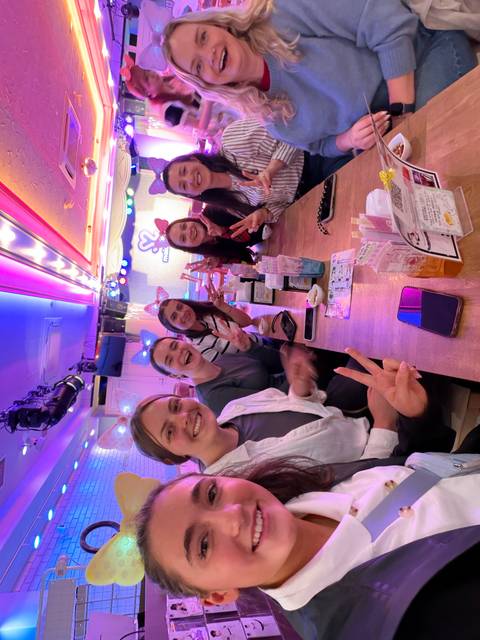       Friends wearing colorful headbands flash peace signs inside a lively themed café with neon lights.
  