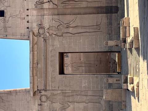       Stone doorway of Philae Temple framed with ancient relief carvings under a blue sky.
  