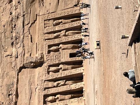       Wide shot of Abu Simbel’s façade with numerous tourists exploring the sandy forecourt.
  