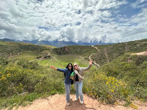       Travellers celebrate with raised arms overlooking the circular agricultural terraces of Moray in the Sacred Valley.
  
