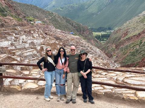       Friends pose before the terraced salt pans of Maras with lush valley backdrop.
  