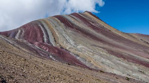       Vibrantly striped slopes of Peru’s Rainbow Mountain rise under a bright blue sky.
  