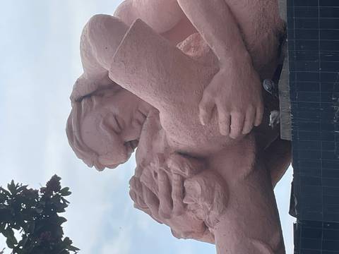       Close-up of the pink stone statue of a kissing couple in Parque del Amor with cloudy sky backdrop.
  