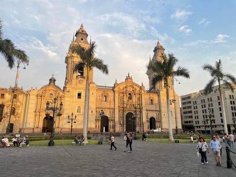       Grand baroque Lima Cathedral dominates Plaza Mayor with palm trees, evening light and locals strolling.
  