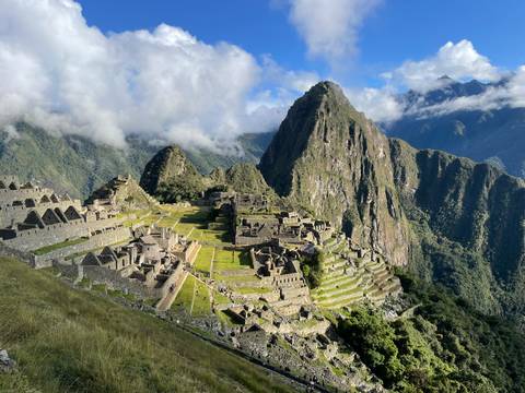       Iconic aerial vista of Machu Picchu citadel perched on green mountain ridge surrounded by cloud forest peaks.
  