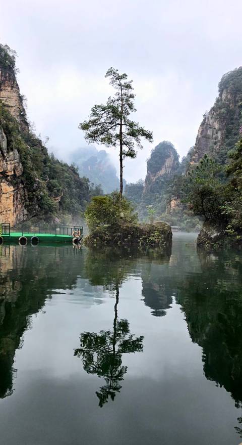       Serene green river flanked by steep karst cliffs and lush vegetation with a small dock and two seated visitors.
  