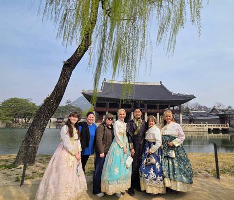       Visitors dressed in colorful hanbok pose beside the pond at Gyeongbokgung’s Gyeonghoeru Pavilion.
  