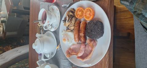       Plate with traditional Scottish breakfast of bacon, sausages, egg, tomatoes and black pudding beside tea.
  