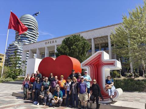       Large tour group poses before a modern opera house with a red heart sculpture.
  