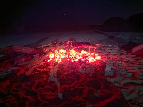       Meat grilling on a metal rack over glowing coals in the desert at night.
  