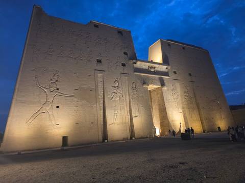       Illuminated pylons of the ancient Temple of Edfu stand against the deep blue twilight sky.
  