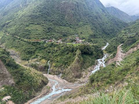       Panoramic view of a deep green valley with a winding river and a small settlement perched on the ridge.
  
