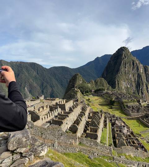       Iconic stone terraces and temples of Machu Picchu with a visitor photographing the scene in the foreground.
  