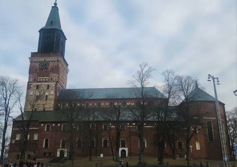       Brick Turku Cathedral with tall clock tower set against an overcast sky and bare winter trees.
  