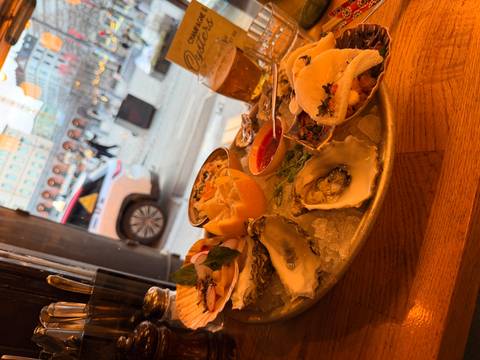       Platter of fresh oysters and assorted seafood with beer on a wooden table inside a bistro
  