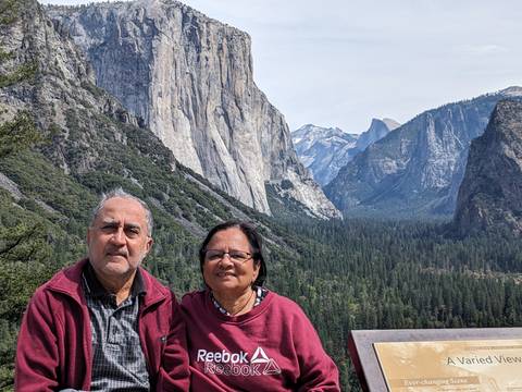       Smiling couple posed at Yosemite’s Tunnel View with El Capitan, Half Dome and dense forest backdrop.
  