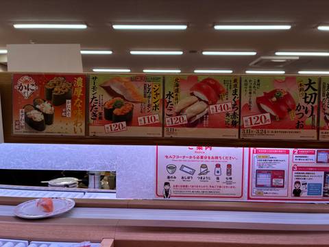       Menu board with photos and prices of sushi selections inside a Japanese conveyor-belt restaurant.
  