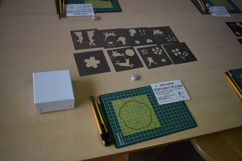       Workshop table displaying stencil templates, cutting mats and craft knives prepared for a class.
  