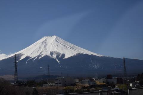       Snow-capped Mount Fuji rises above the plains with power lines in the foreground under clear skies.
  