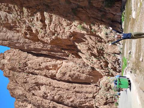       Traveler raising arms at the base of towering red rock walls in Todra Gorge.
  