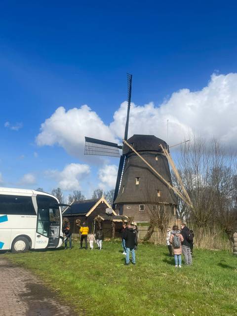       Traditional Dutch windmill towers above a tour bus under a bright blue sky with fluffy clouds.
  