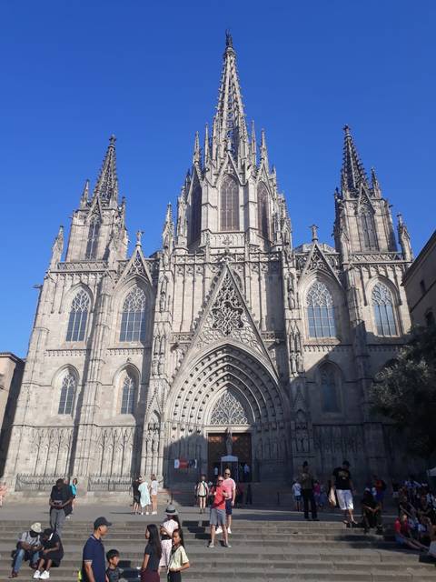       Gothic façade of Barcelona Cathedral stands tall against a clear blue sky.
  
