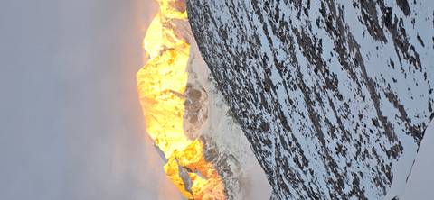       Close vertical view of a sun-lit Himalayan peak glowing orange at dusk.
  