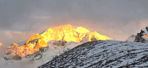       Panoramic sunset light bathes a dramatic snow-covered Himalayan peak above a ridgeline.
  