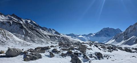       Snow-blanketed high-altitude valley with boulder-strewn foreground below sharp Himalayan peaks.
  