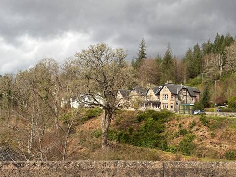       Stone country house and bus stop nestle among bare oaks and evergreens under grey skies.
  