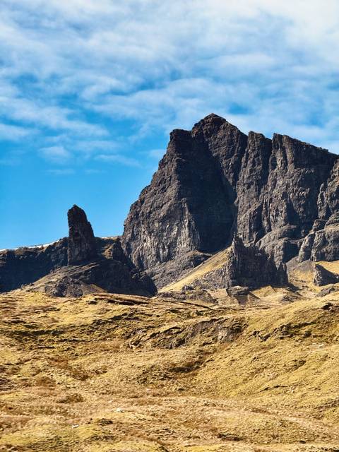       Dark basalt spires of the Old Man of Storr rise dramatically above yellow moorland.
  