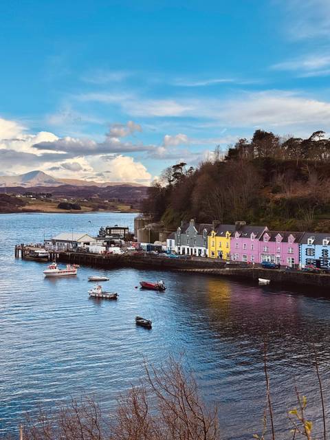       Colorful row of houses lines Portree’s waterfront with boats bobbing in the bay.
  