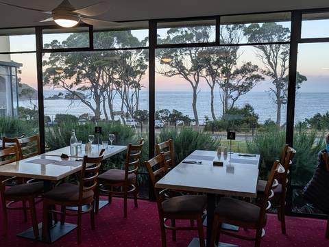       Restaurant dining room overlooks gum trees and the sea through large picture windows.
  