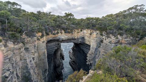       Natural sea arch carved into high sandstone cliffs with churning ocean below.
  