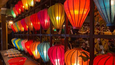       A row of brightly colored silk lanterns glows inside a bustling Hoi An restaurant at night.
  